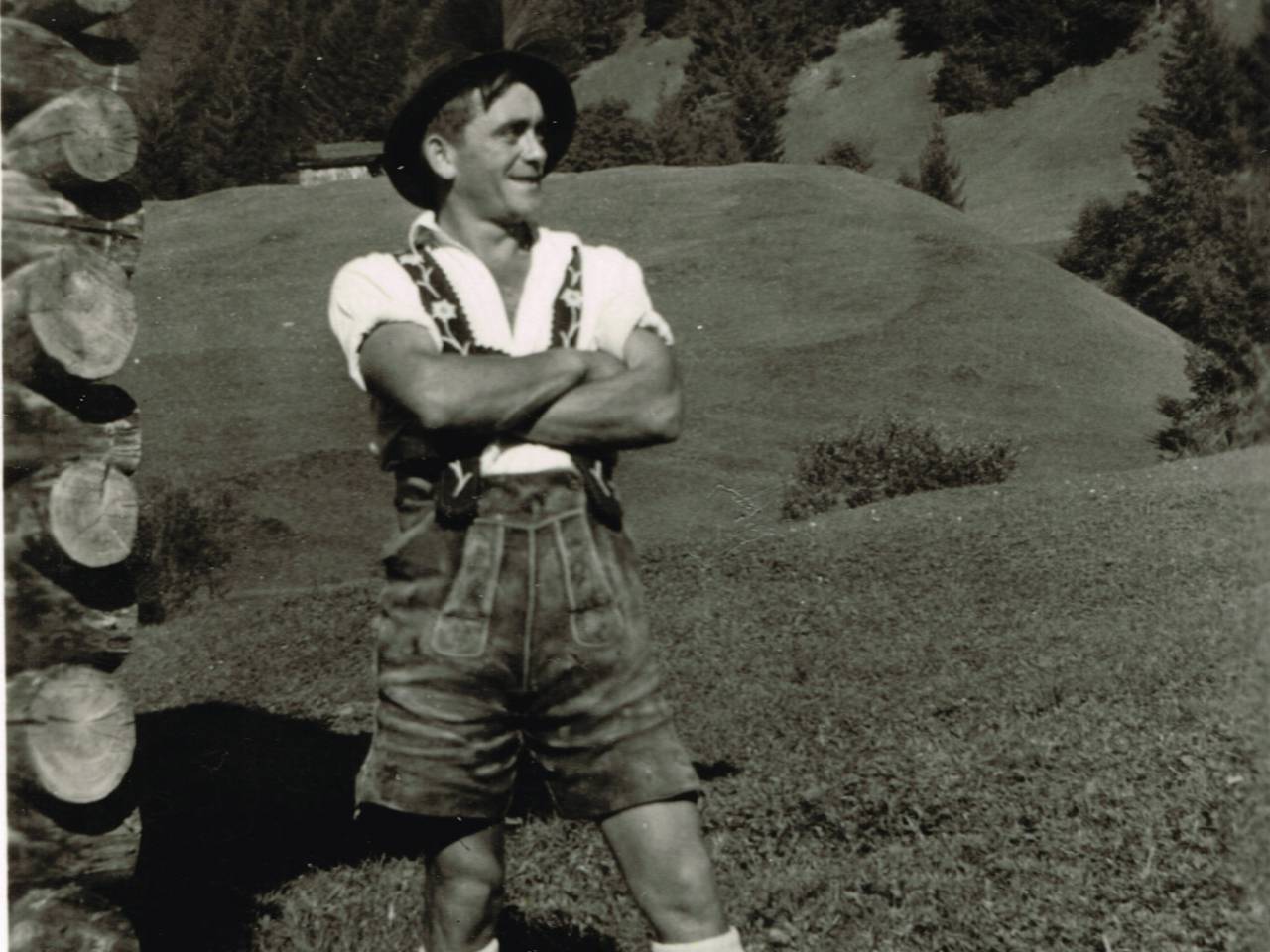 Mann in Ledertracht steht neben Berghütte