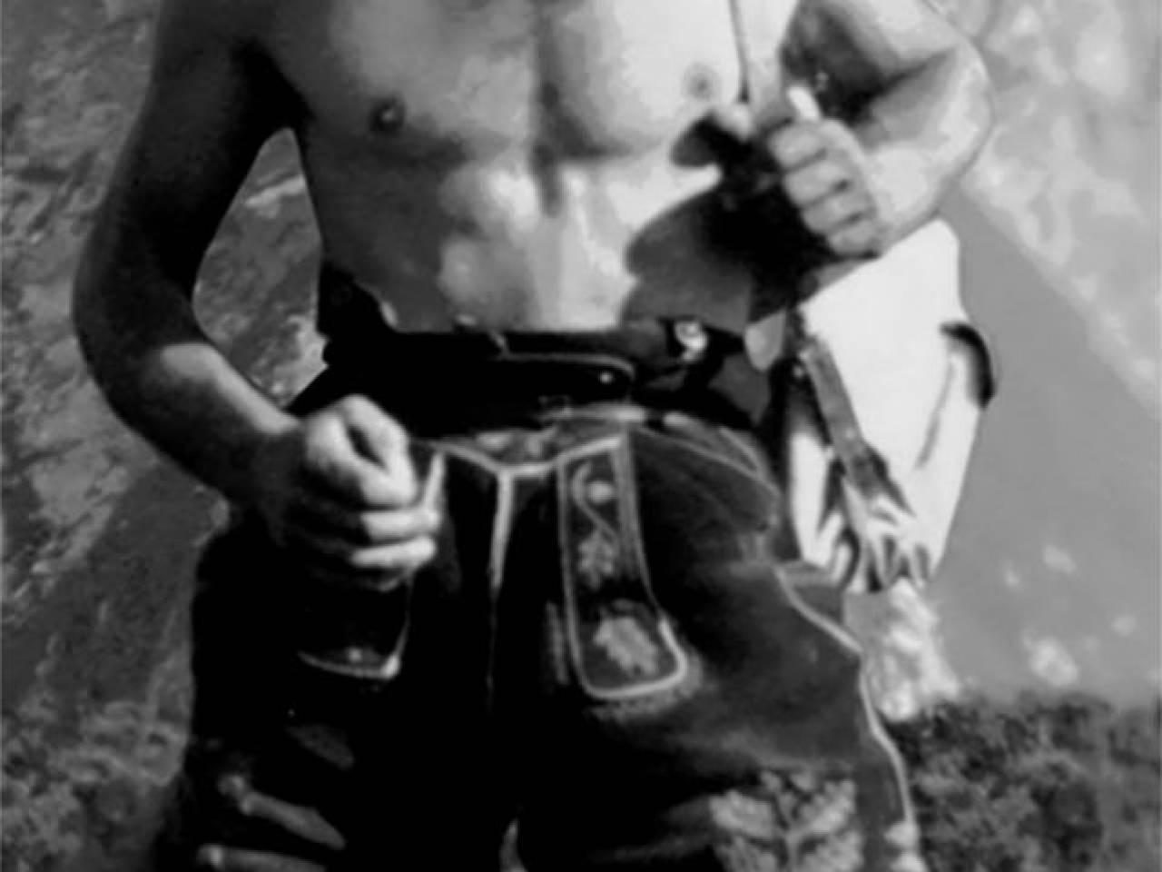 Mann in Lederhose steht auf Bergwiese Schwarz Weiß Bild