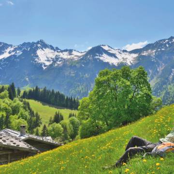 Man liegt in Bergwiese umgeben von Bergpanorama